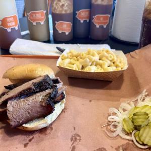 Barbecue brisket sandwich with mac and cheese, pickles, and onions on brown paper.